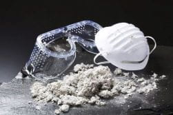 Safety goggles and N-95 mask with small pile of asbestos