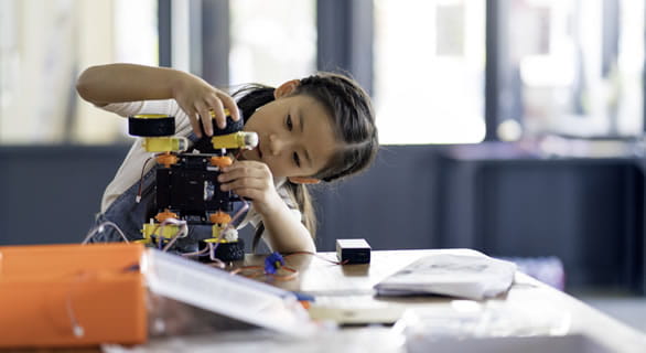young girl at a table working on a robot