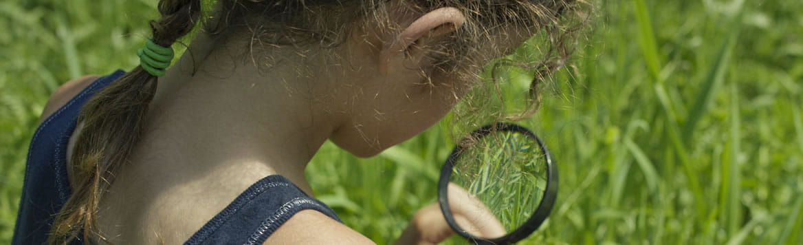 young child outside looking at something through a magnifying glass