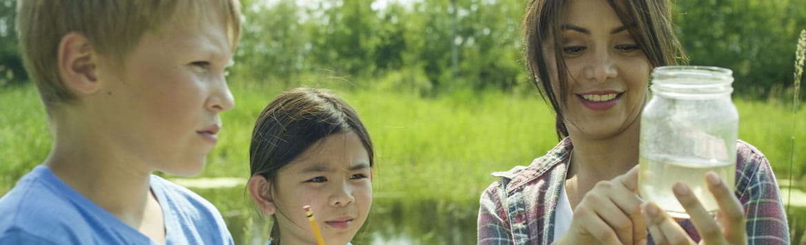 teacher outside holding jar of freshwater while two young students observe it
