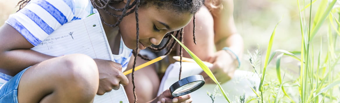 girl outside using magnifying glass to look at glass