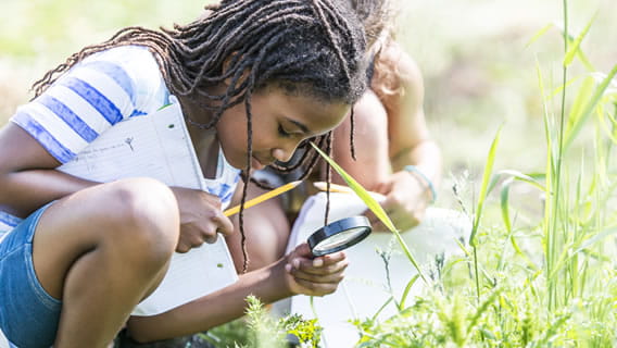 young girl outside looking at plants through a magnifying glass