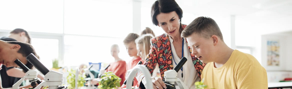 teacher in classroom lab with students looking through microscopes