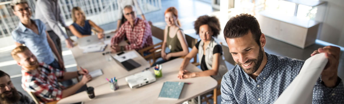 seven coworkers sitting at a table watching a presenter write something on an easel pad