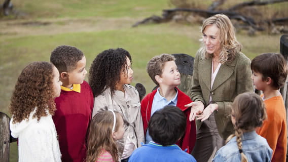 teacher outside discussing something with eight young children