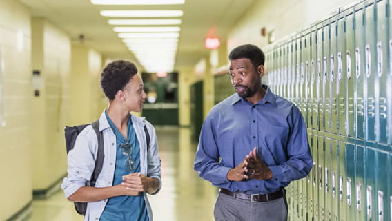 student and teen student talking while walking down the hall next to lockers