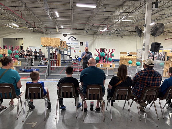 Region 9 Director Brian Dotson speaks to an audience at MiSTEM's FIRST Robotics grand opening with the robotics setups featured behind him