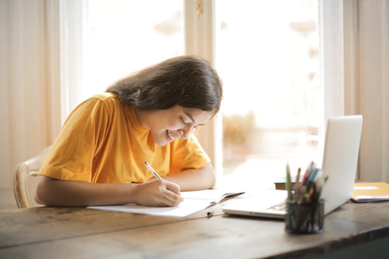 Female student writing with laptop on table