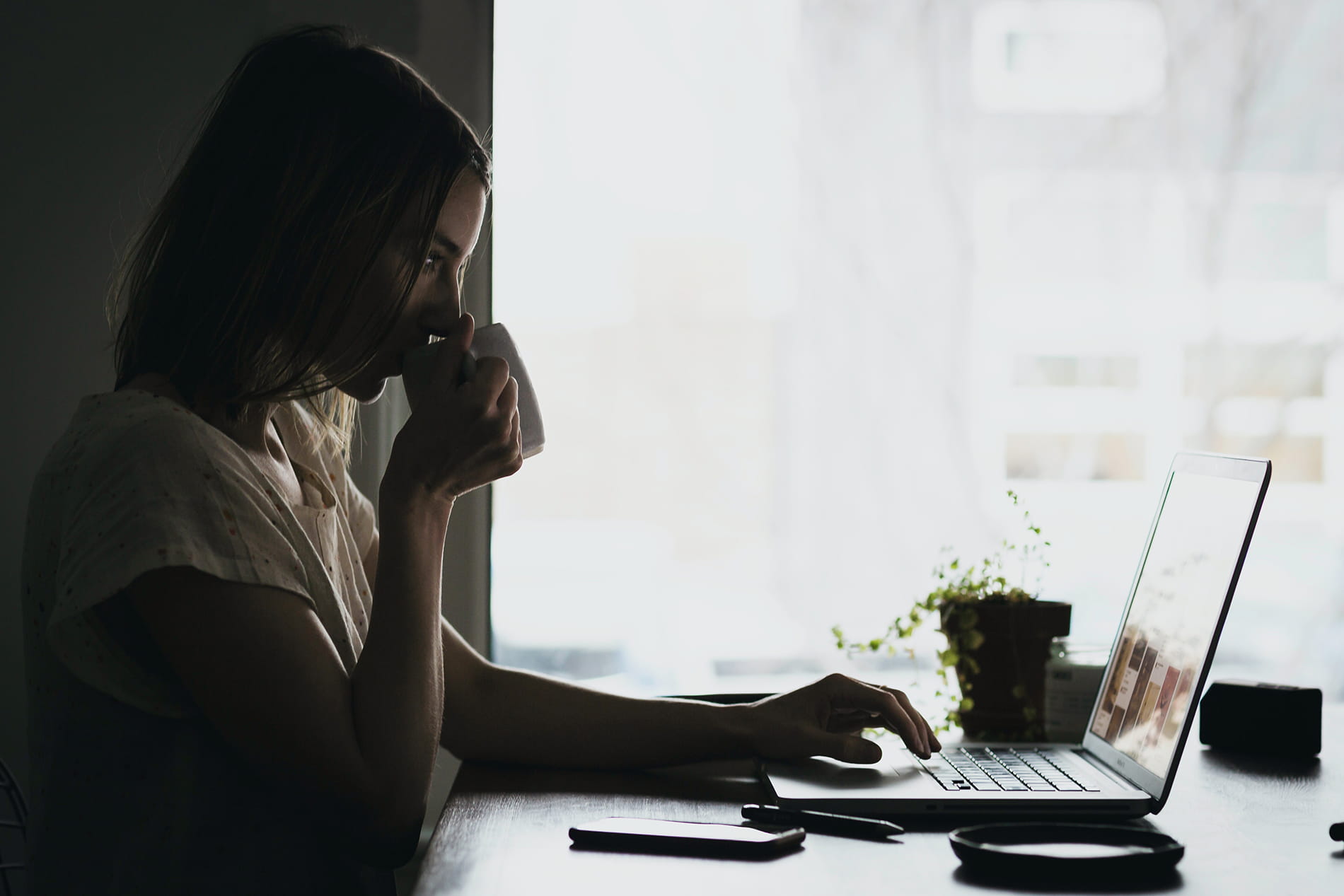 Adult drinking from cup looking at computer 