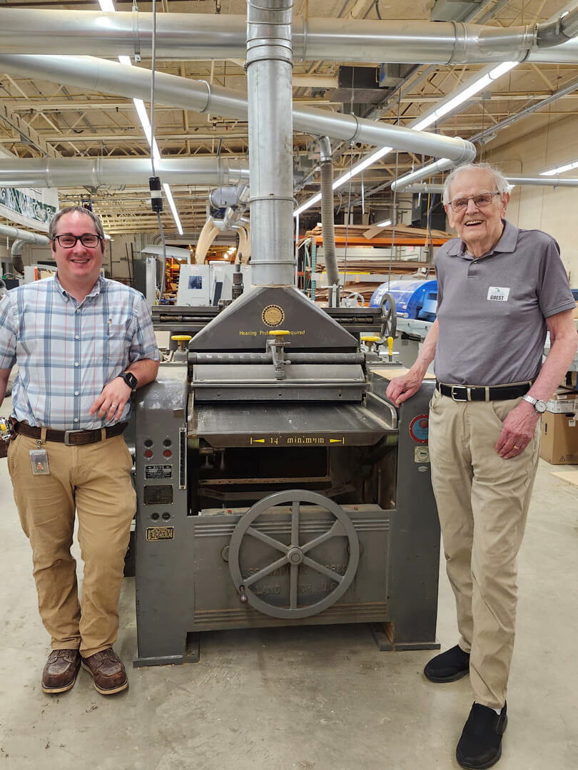 MCTI 1963 alumnus Garrett Mulder (right) and current cabinetmaking instructor Matt Glave standing next to machinery used by Mr. Mulder when he attended Michigan Career and Technical Institute.
