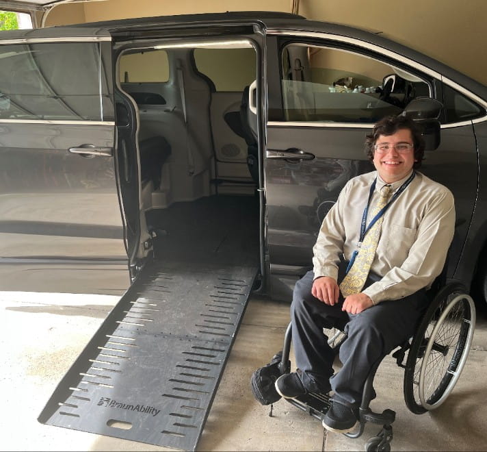 Benjamin, a white man in a wheelchair, sitting next to an accessible van with the side ramp open.