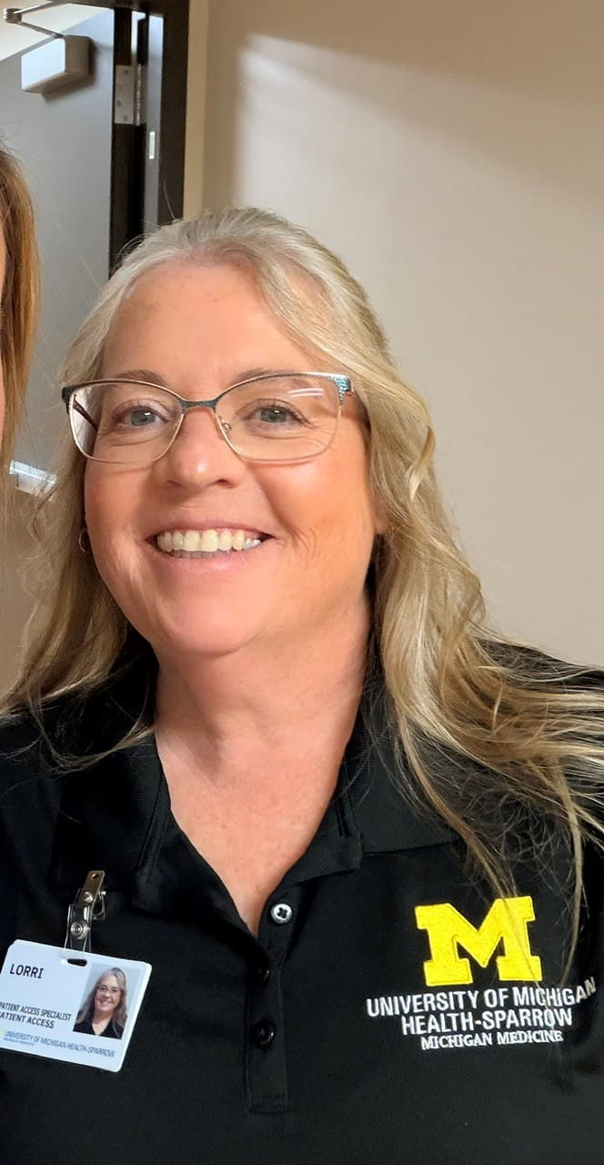Lorri, a white woman with blonde hair and glasses, wearing a University of Michigan shirt.