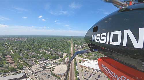 Aerial view from a Mission-branded aircraft flying over a city and roadway.