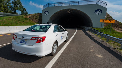 White sedan approaching the entrance of a vehicle test tunnel on a closed roadway.