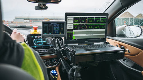 Interior of a test vehicle with monitoring equipment and a laptop displaying vehicle and sensor data.