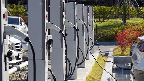 Row of electric vehicle charging stations with cars parked beside them.