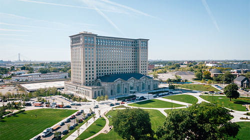 Aerial view of Michigan Central Station with surrounding streets, lawns, and city buildings.
