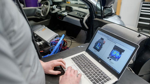 Person using a laptop to review vehicle mobility data next to a test vehicle in a lab setting.