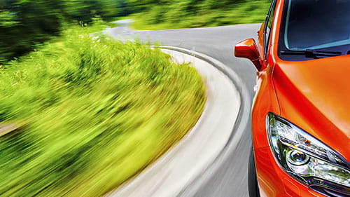 Orange car driving along a winding road bordered by green vegetation.