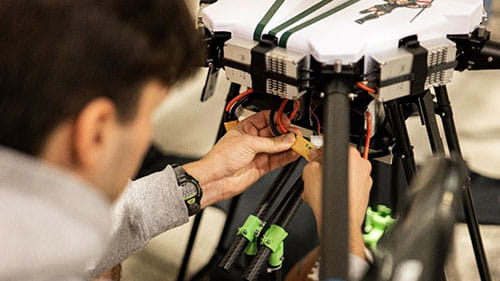 Researcher adjusting wiring on a large drone or autonomous aircraft in a lab setting.