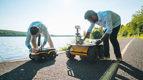 Two people testing small autonomous mobility devices along a lakeside road.