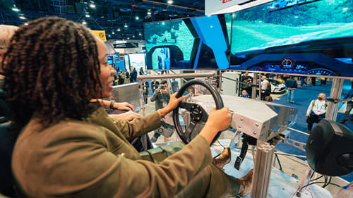 Person using a driving simulator at a mobility technology event.