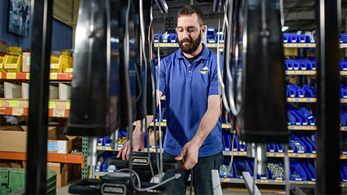 Technician working on a large drone or prototype aircraft in a workshop with parts shelves in the background.