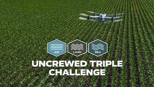 A drone flies above a farm field with Uncrewed Triple Challenge branding for air, land, and sea.