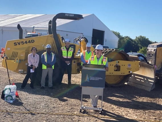Speaker at a podium at a construction site while others stand behind