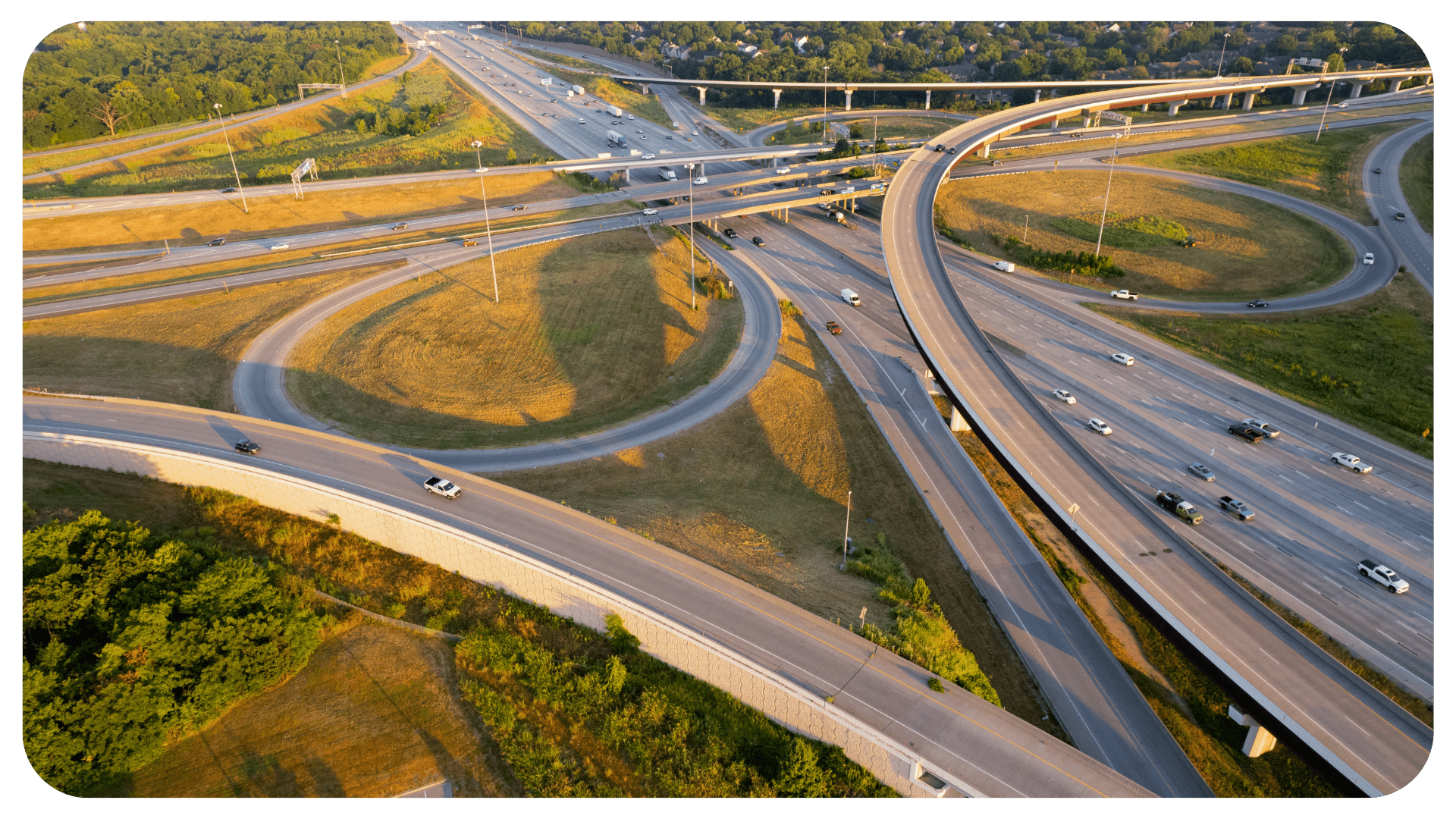 An aerial view of cars on a freeway. The freeway is surrounded by green grass and trees.