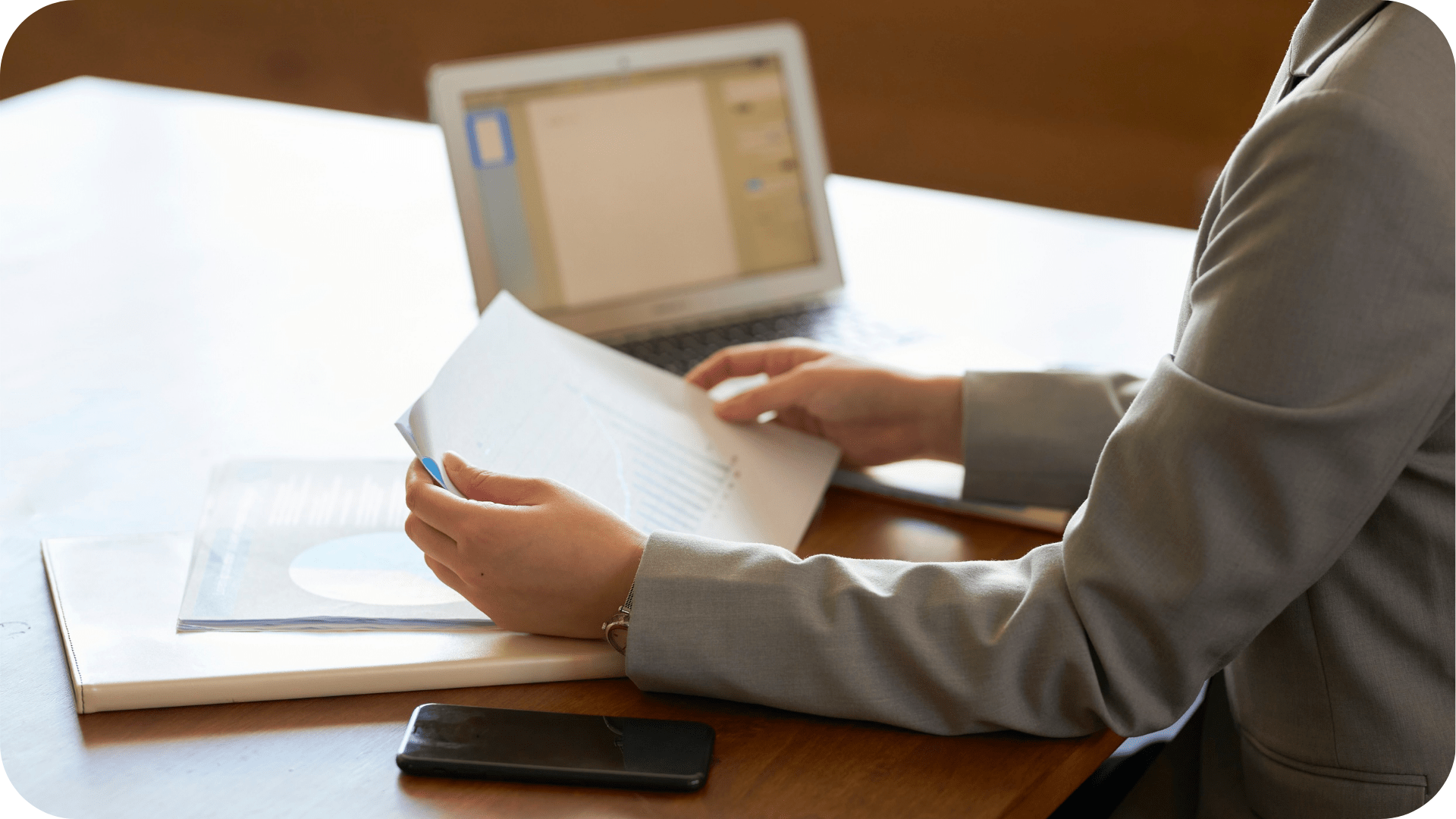 A pair of hands holding a document. There is a laptop in the background.