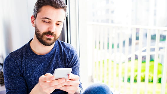 hipster-businessman-in-blue-long-sleeved-t-shirt-working-from-home-holding-smart-phone