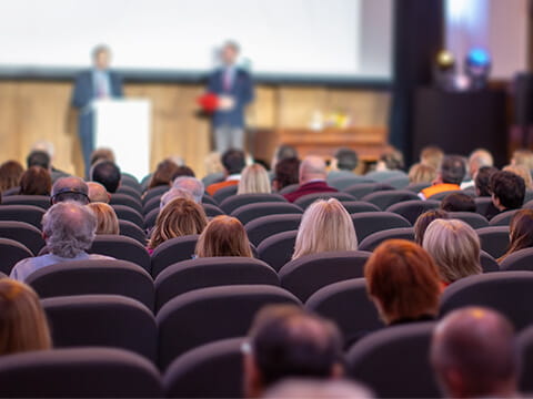 People sitting in auditorium seats while watching a professional presentation onstage during a seminar.