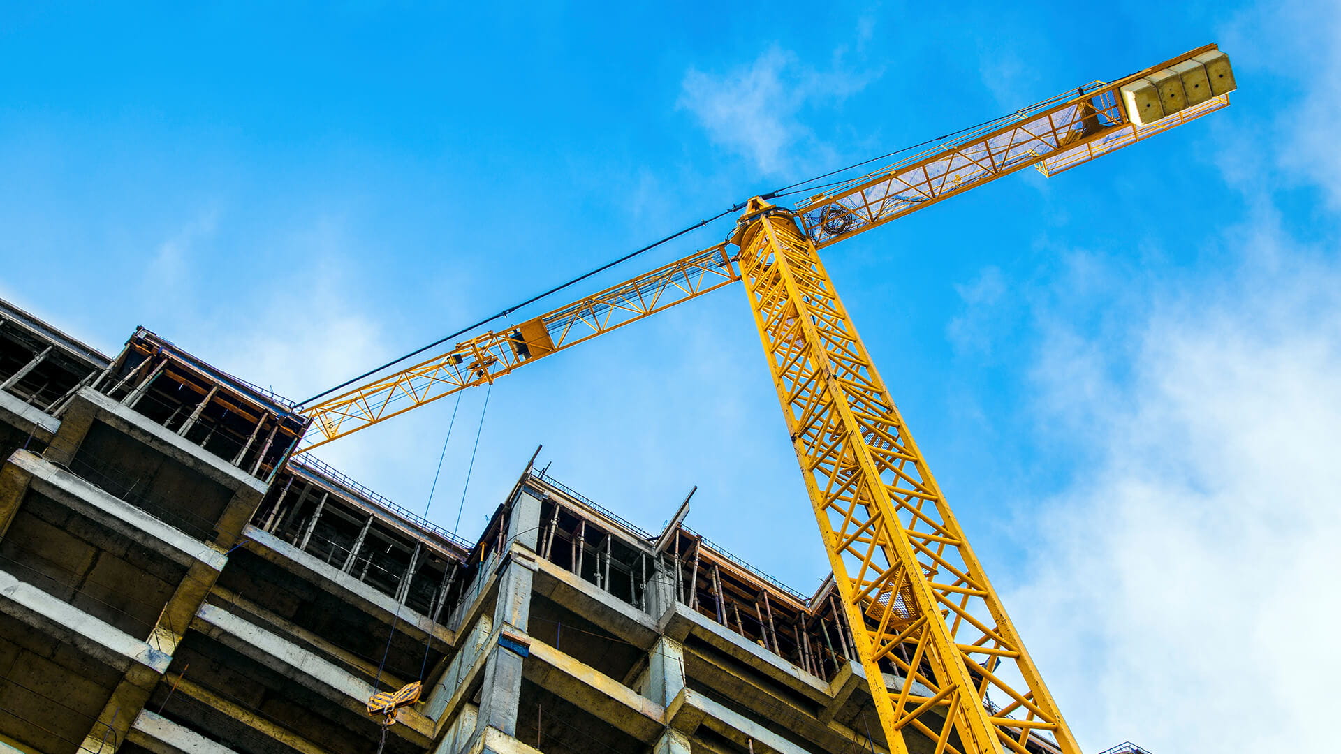 Tower crane operating above a multi-story building under construction against a blue sky.