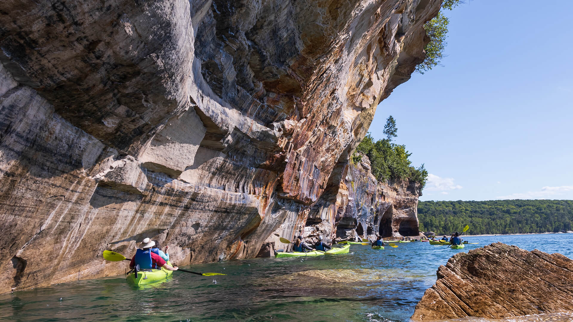 People kayaking along rocky cliffs on a lake during an outdoor recreation excursion.