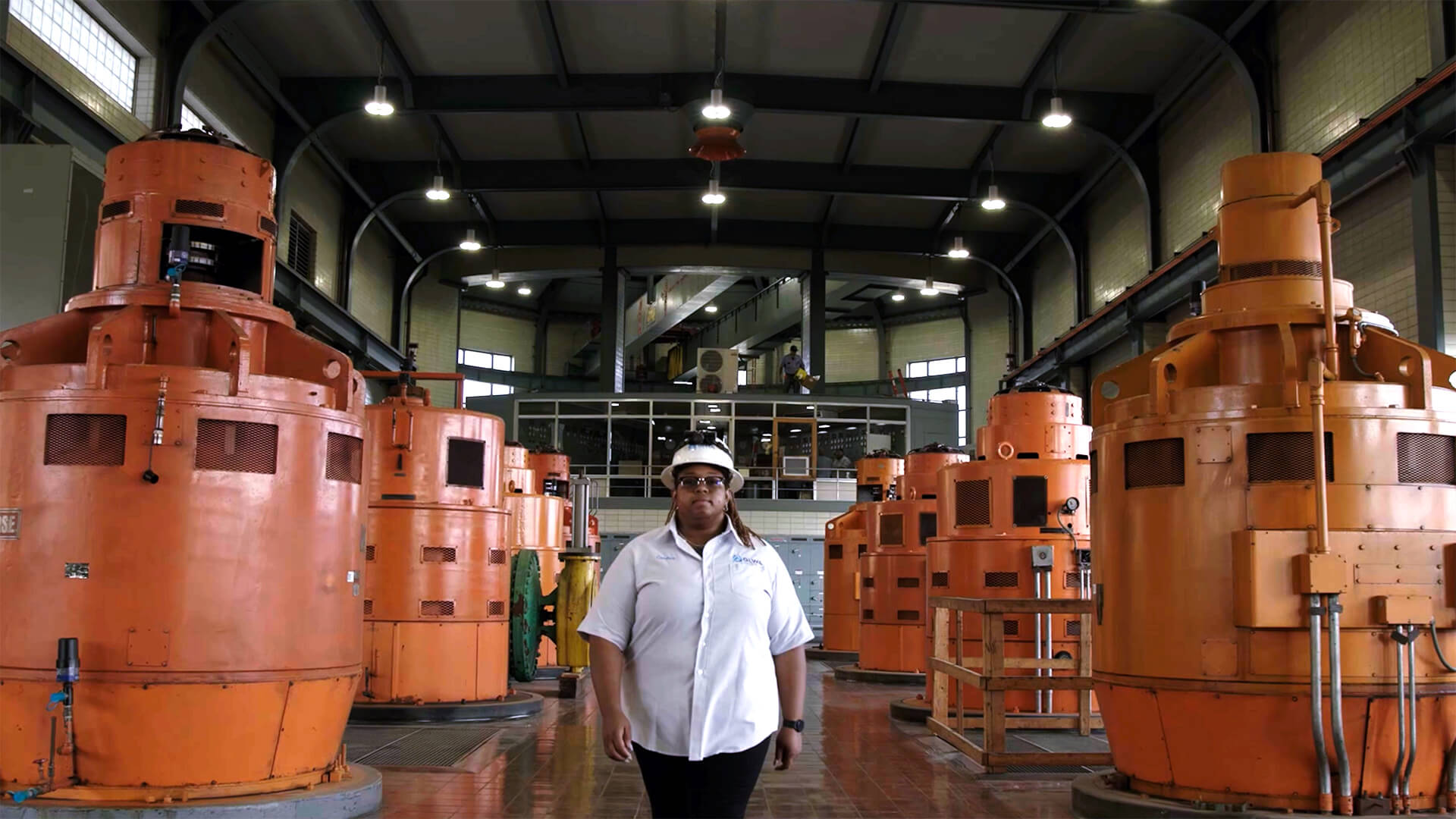 Person in safety gear standing among large orange industrial machines.