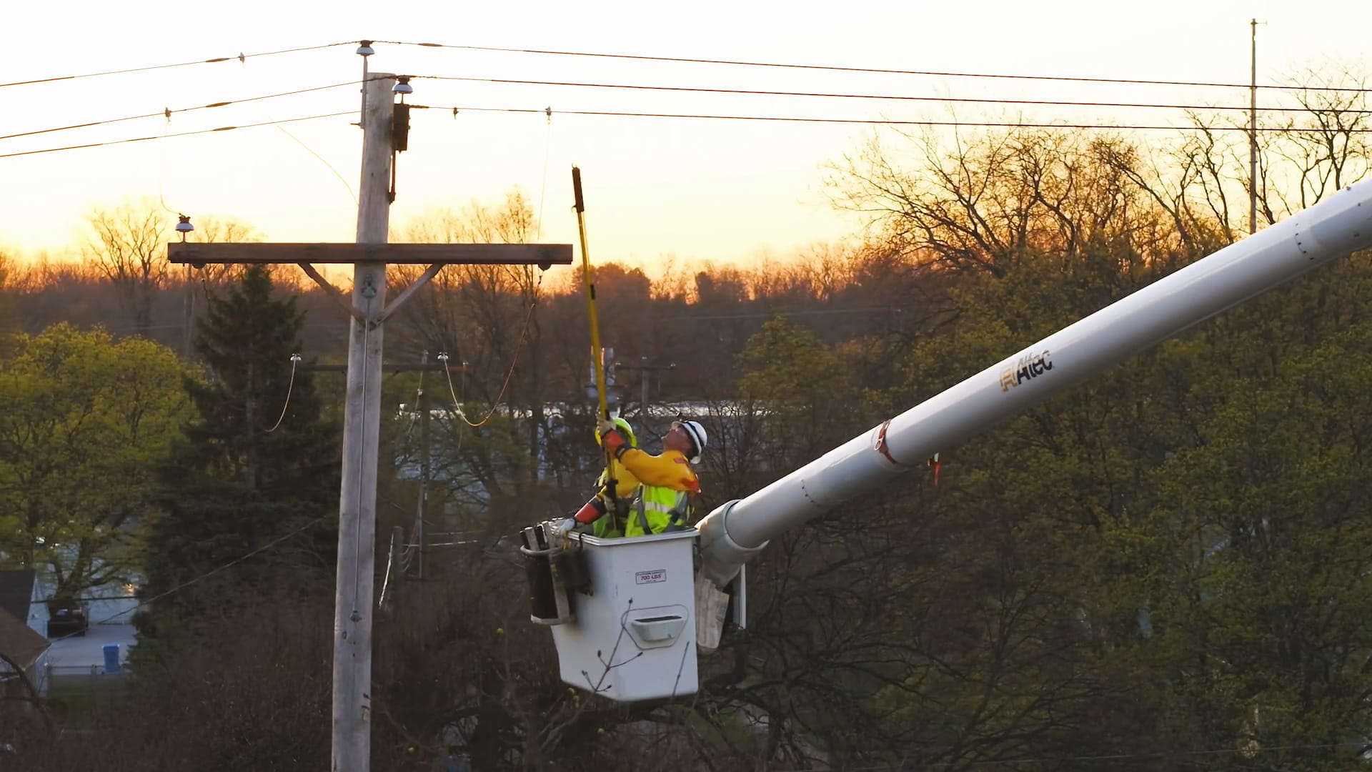 Two utility workers wearing high-visibility safety vests and hard hats operate from a bucket truck to perform maintenance on overhead power lines — demonstrating hands-on training in a Registered Apprenticeship Program for employers.