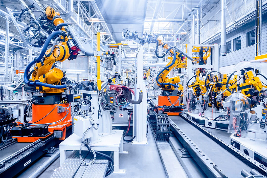 Automated robotic arms operate along a production line inside a modern manufacturing facility, assembling components in an advanced industrial workspace.