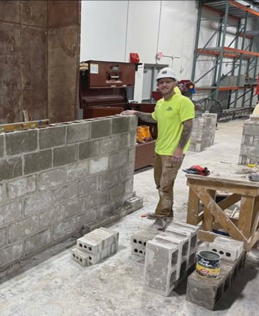 Lucas wearing a hardhat and standing inside a building next to building materials