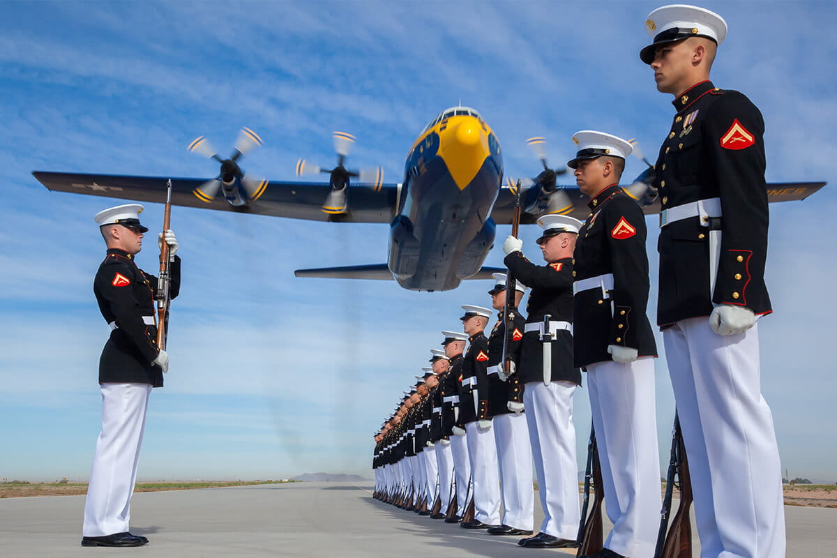 Row of U.S. Marines standing at attention with a plane flying overhead.