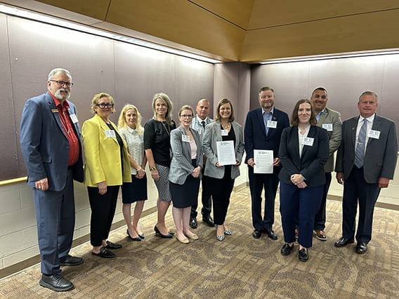 ten people in business dress clothes stand side by side smiling with two near the middle holding up certificates