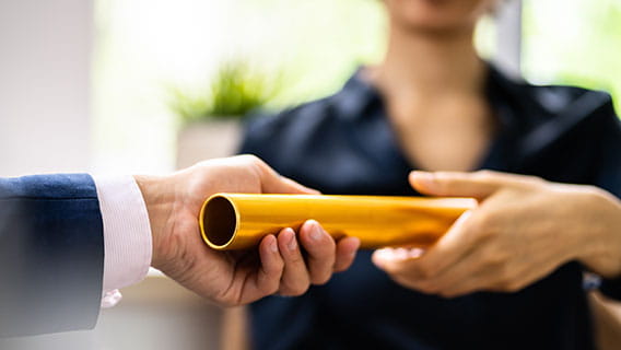 the hands of a person in business clothes passing a baton to another person in business clothes