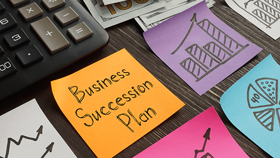 a desk with a keyboard, money, and sticky notes, and one sticky reads business succession planning