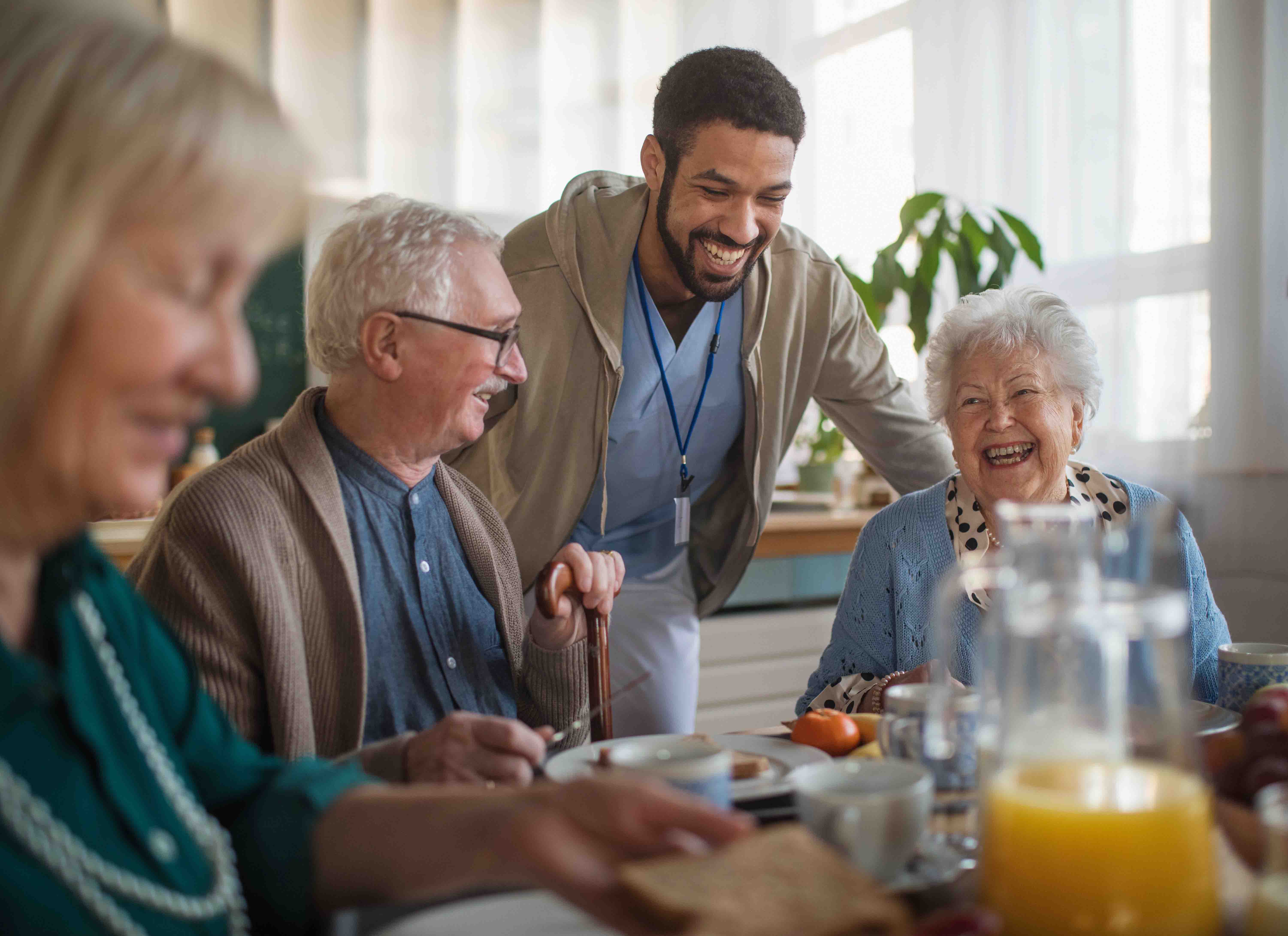 nursing care facility worker smiling and interacting with residents seated at a table