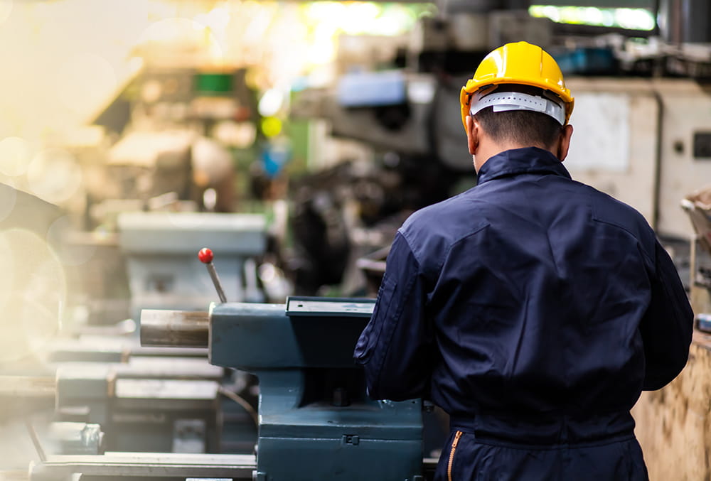The back of a man wearing a hard hat and uniform working on a machine in a factory