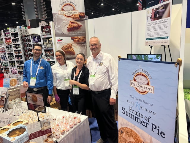 Grand Travers Pie Company posing together behind their booth at a trade show in Chicago in 2024.