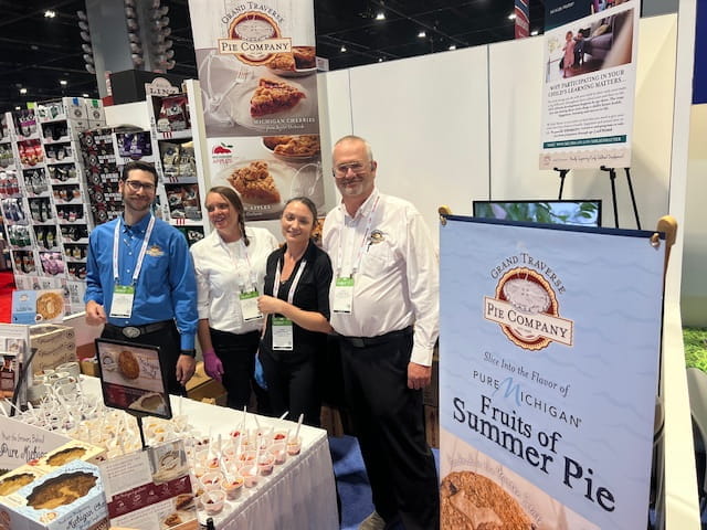 Grand Travers Pie Company posing together behind their booth at a trade show in Chicago in 2024.
