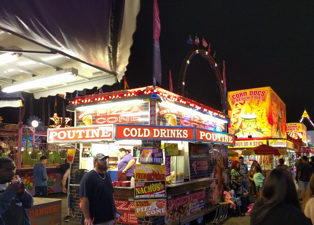 Night time view of a county fair. Brightly colored signs of vendors selling food