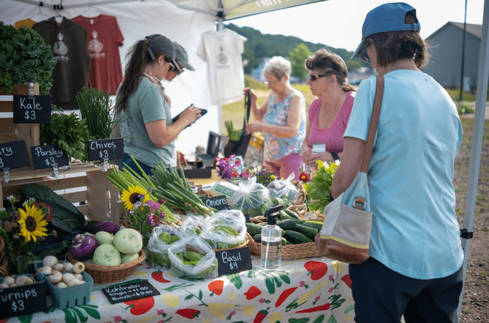 A vegetable and herb seller at a farmers market with a few customers.