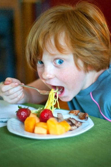 A kid eating spaghetti and fruit for lunch.